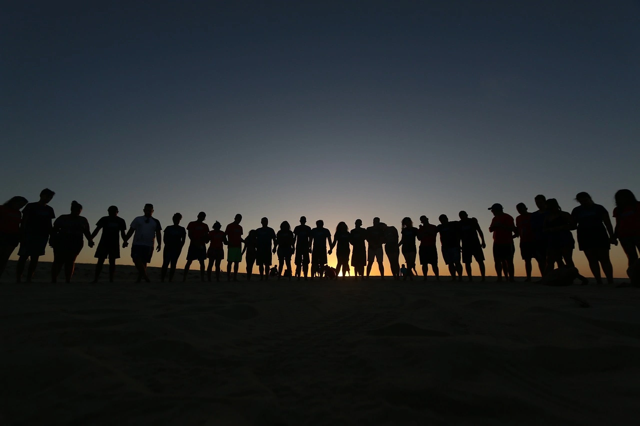 Ronde de femmes et d' hommes se donnant la main au coucher du soleil